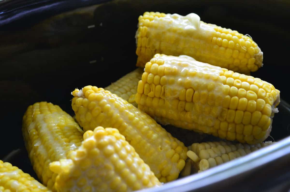 Half ears of cooked corn on the cob drizzled in butter in a black pot. 