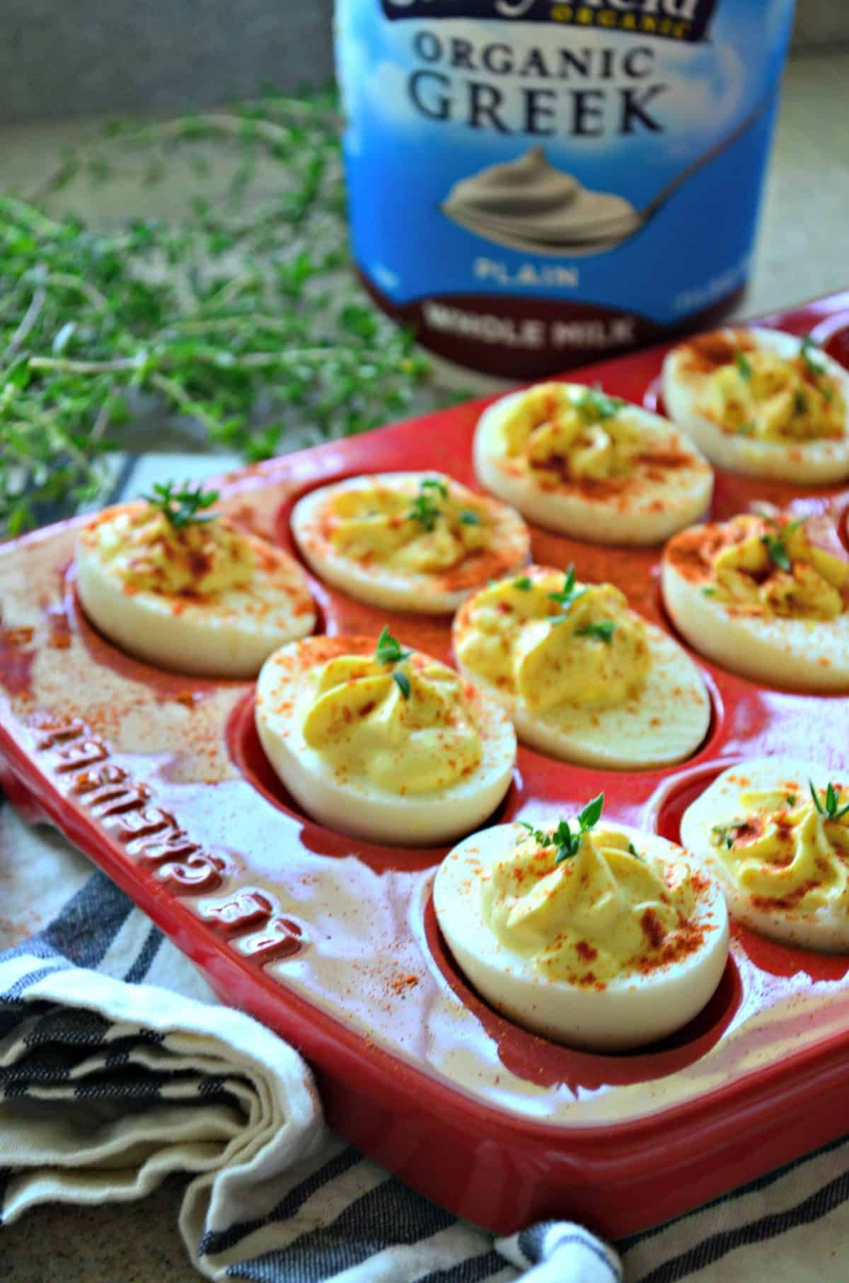 closeup top view of deviled eggs sprinkled with paprika in red egg holder in front of greek yogurt.
