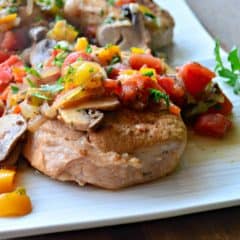 White plate filled with two italian pork chops with peppers, tomatoes, and mushrooms.