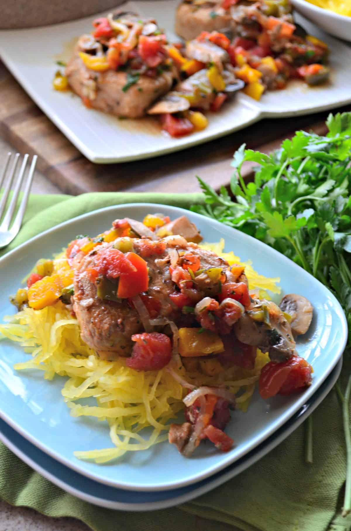 closeup top view of pork chops covered in herbs, tomatoes, mushrooms, over spaghetti squash.