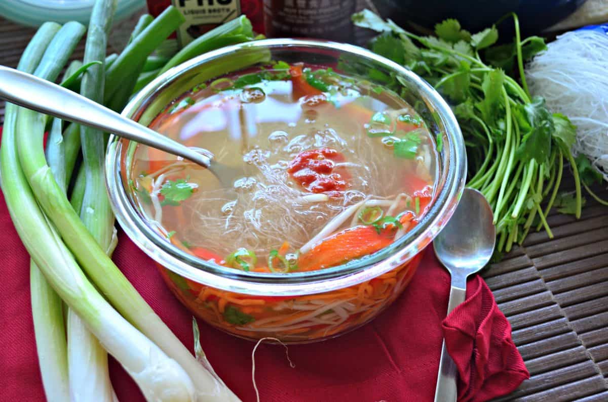 top view glass container filled with sliced peppers, rice noodles, cilantro, broth, and bean sprouts.