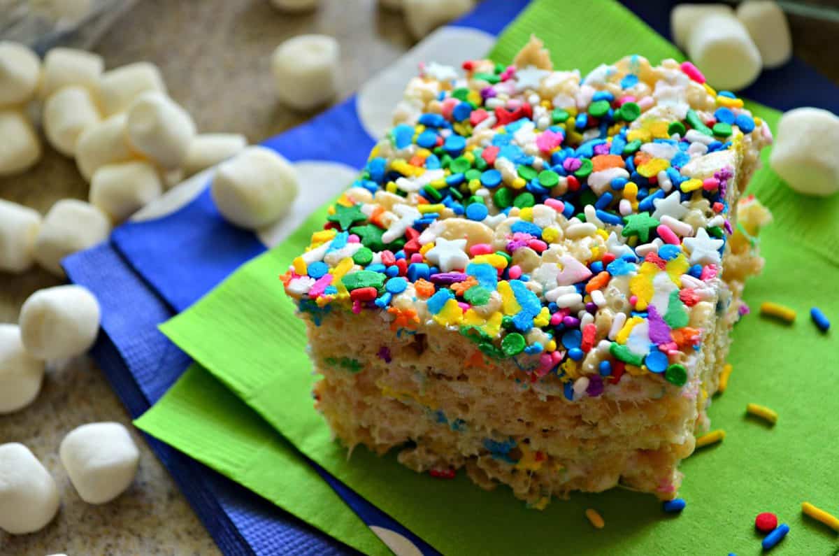 closeup of colorful sprinkle topped rice crispy square on green napkin with mini marshmallows and title text.