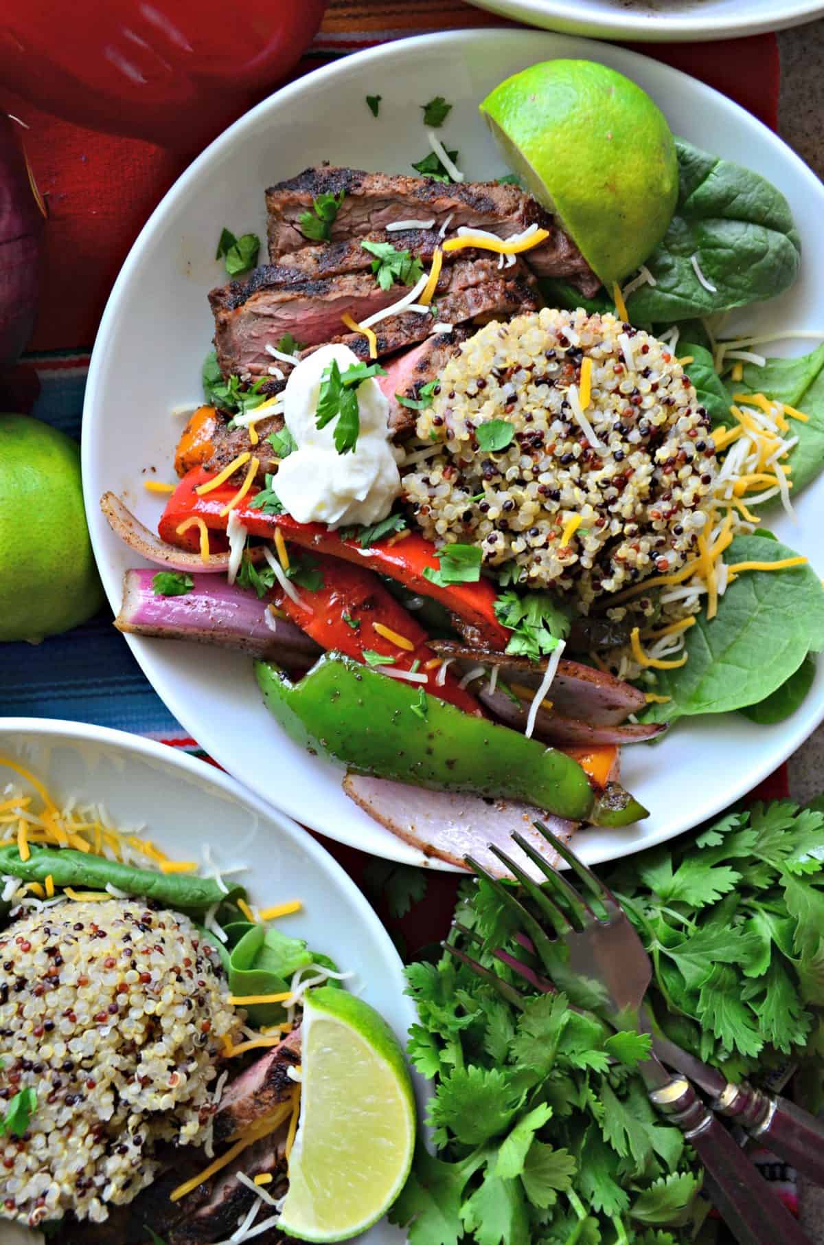 side view of white bowl with quinoa, grilled onions and peppers, steak, cilantro, and sour cream.