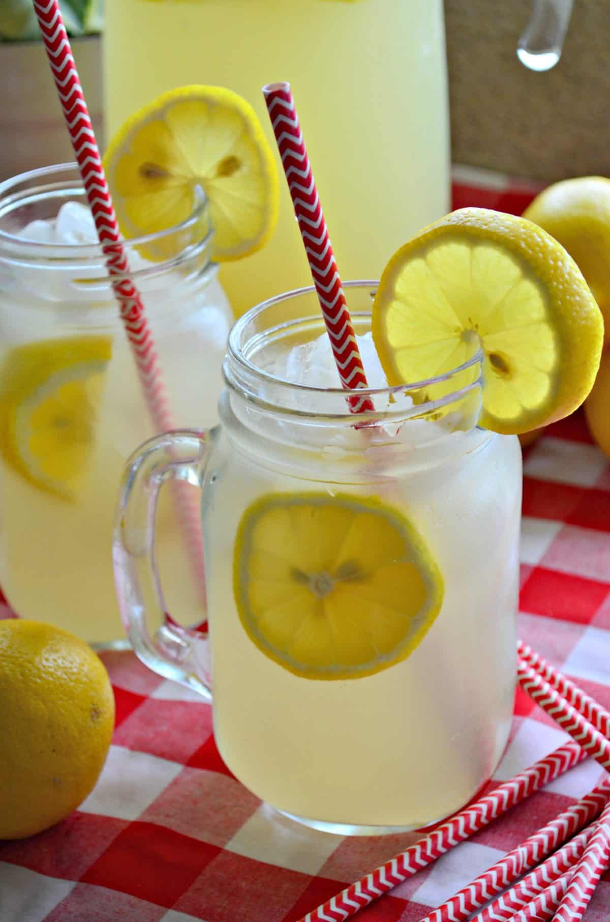 Closeup side view of lemonade in two mason jars with fresh lemon wheels and red straws.