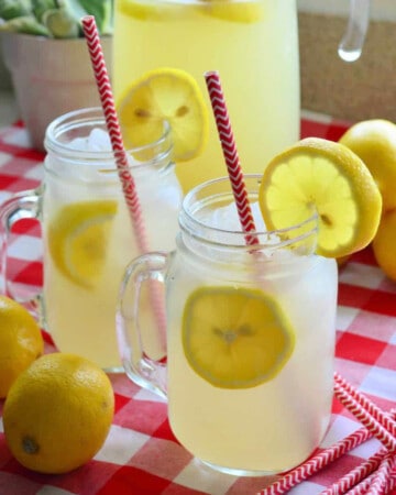 Two mason jars filled with lemon slices and lemonade on a red and white checkered cloth.