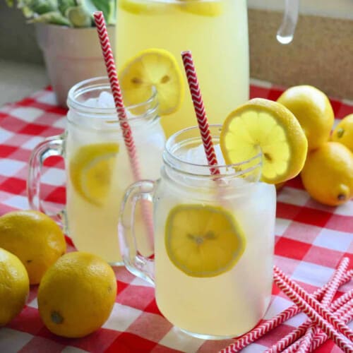Two mason jars filled with lemon slices and lemonade on a red and white checkered cloth.