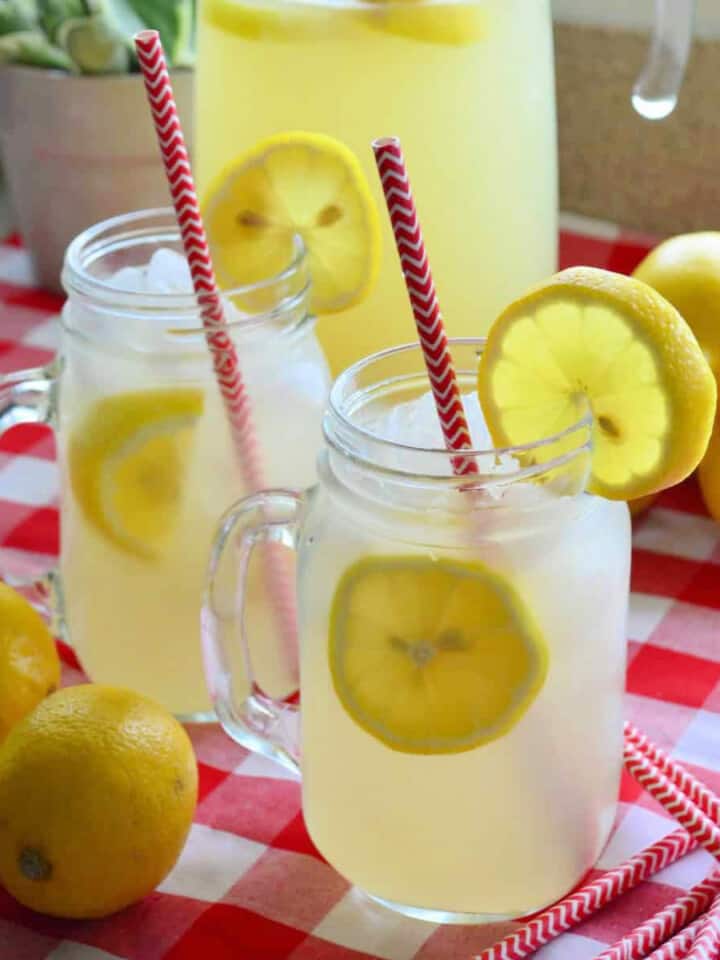 Two mason jars filled with lemon slices and lemonade on a red and white checkered cloth.