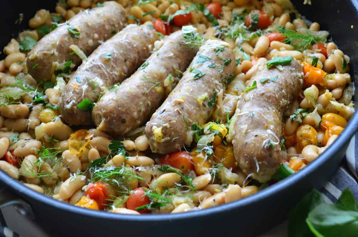 Black skillet with white beans, tomatoes, and fresh herbs. 