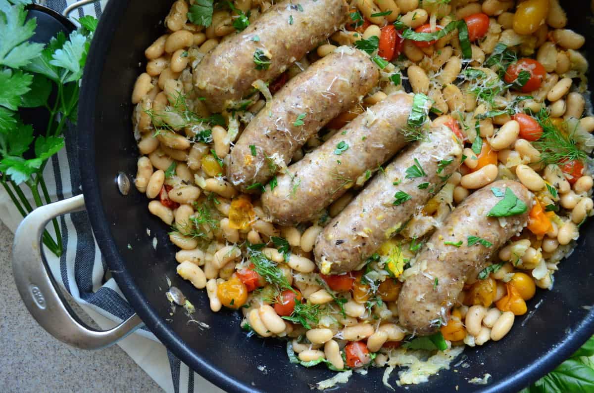 top view of 5 sausages in skillet over beans with basil and cheese next to parsley.