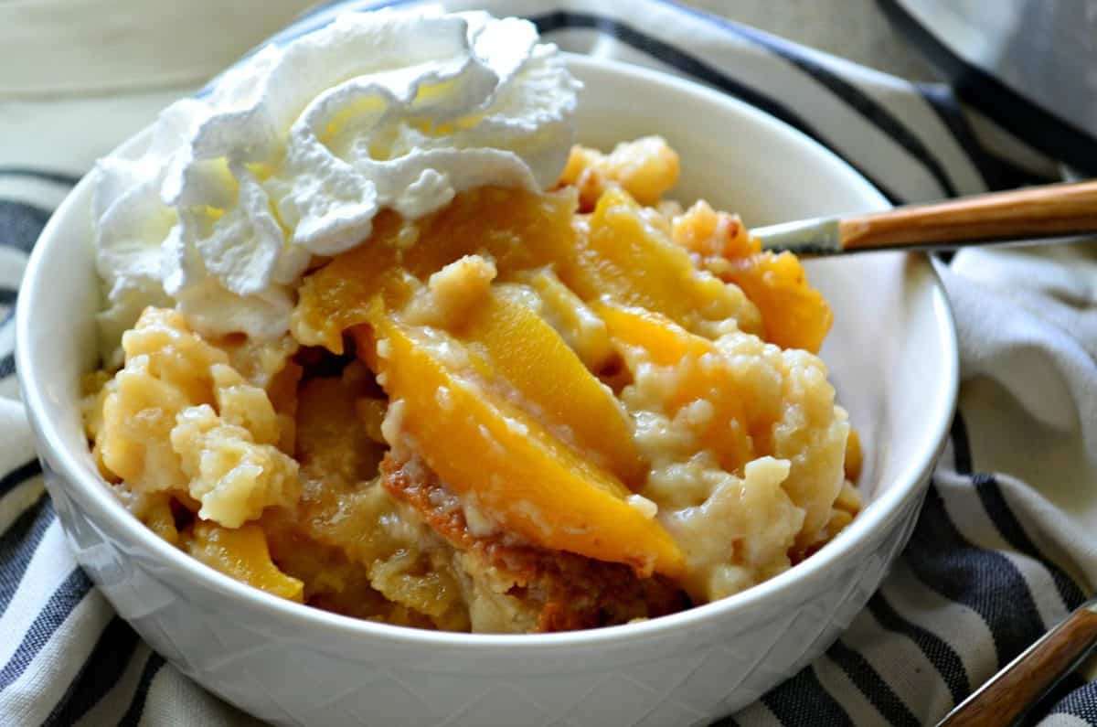 Top view of white dish filled with peach slices, whipped cream, and cobbler with title text.
