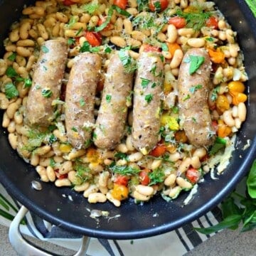 Black skillet with sausage links and white beans with fresh herbs.