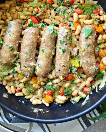Black skillet with sausage links and white beans with fresh herbs.
