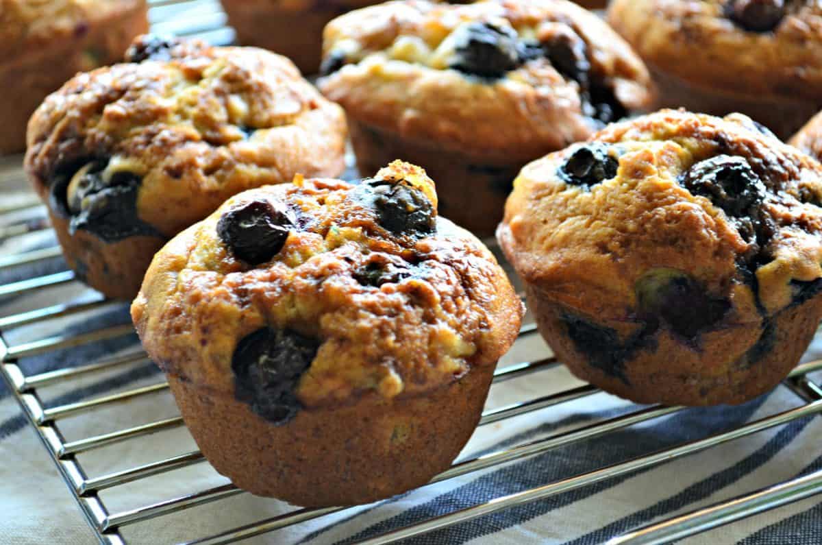 closeup side view of Banana Blueberry Muffins on metal resting rack with title text.