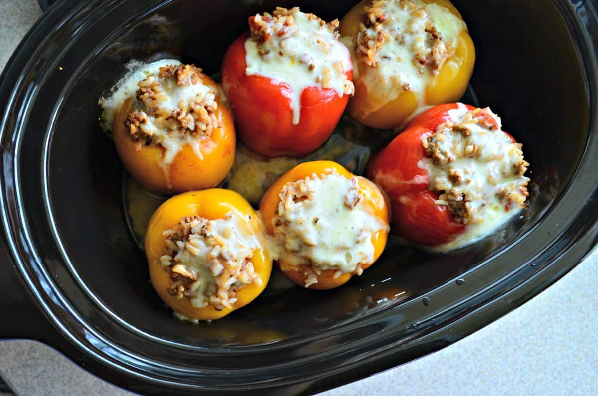 top view of 6 bell peppers stuffed with rice and meat, topped with cheese in slow cooker.