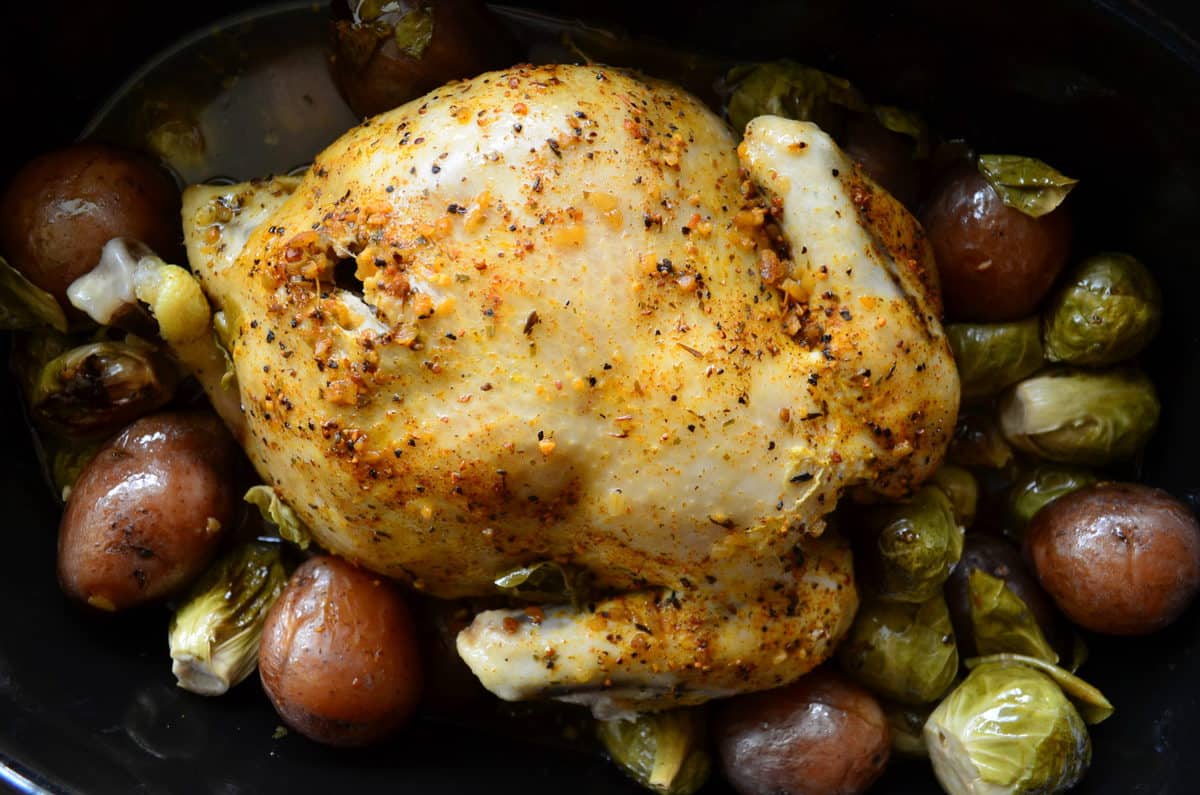 Top view of Golden browned chicken topped with herbs in slow cooker with potatoes and brussels sprouts.