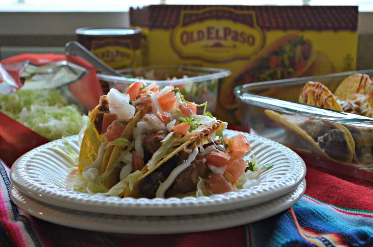 Beef & Refried Bean Baked Tacos stacked on a white plate covered in lettuce and diced tomatoes.