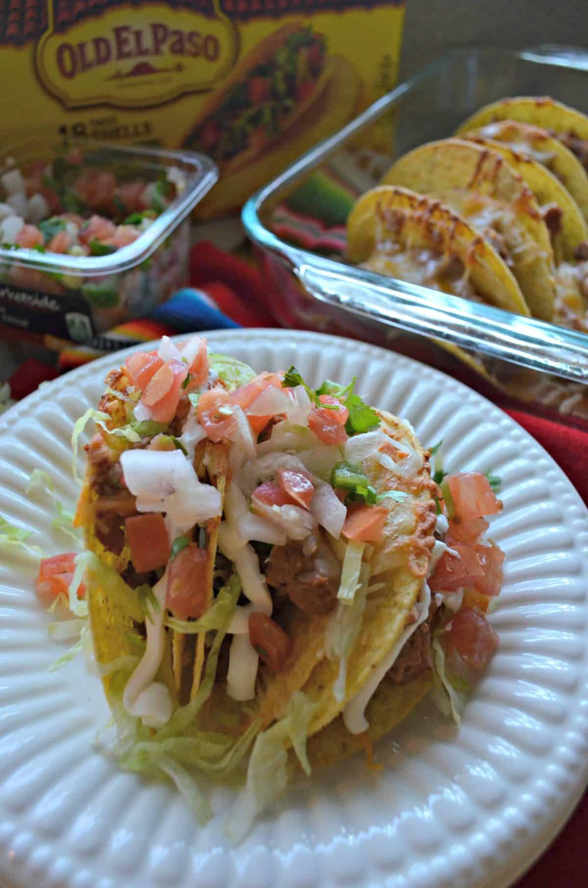 Beef & Refried Bean Baked Tacos stacked on a white plate covered in lettuce and diced tomatoes.