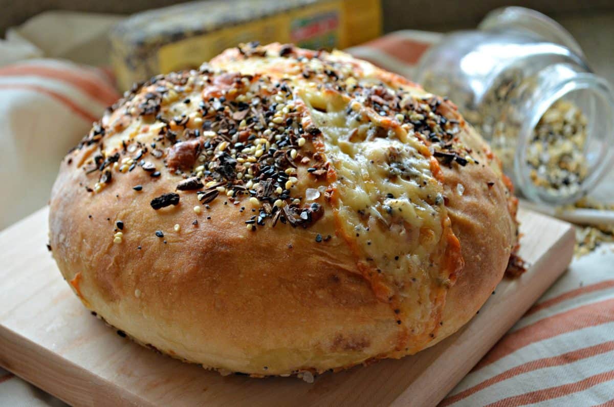 closeup of Cheesy No-Knead Crusty White Bread sprinkled with everything bagel seasoning on wooden slab.