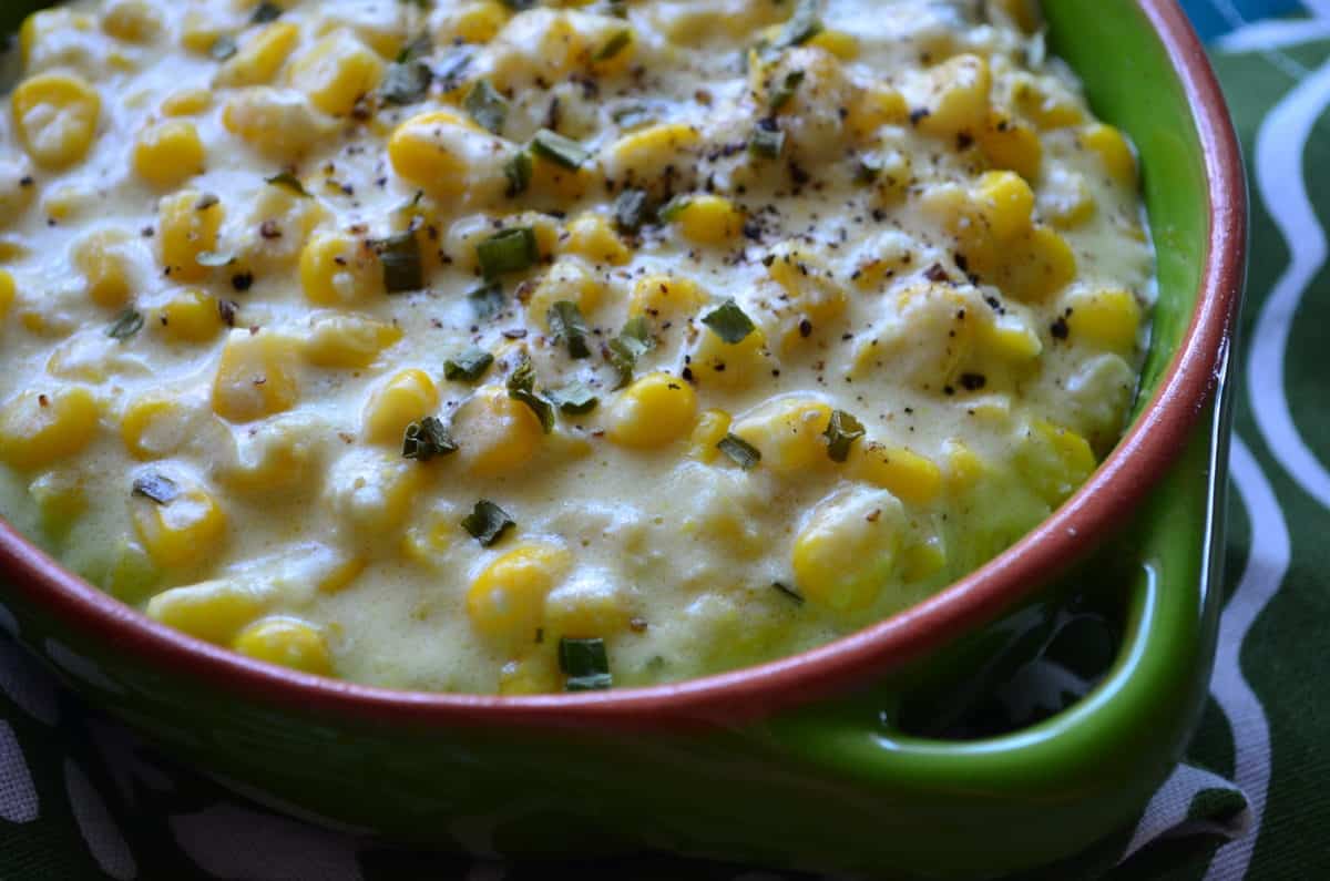 closeup of creamed corn topped with spices and herbs in green bowl.