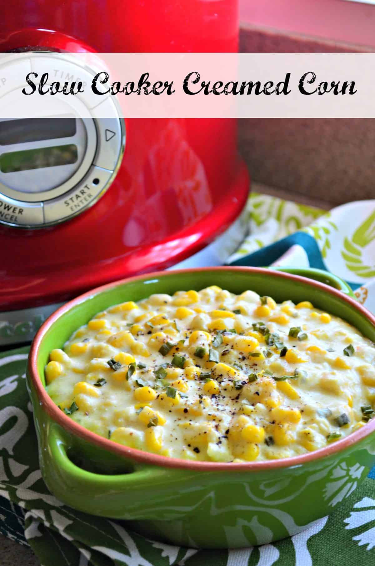 creamed corn topped with spices and herbs in green bowl in front of red slow cooker with title text.