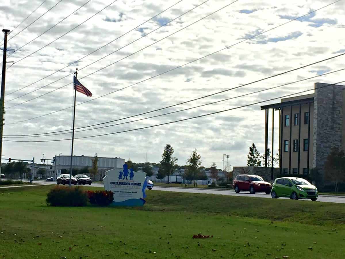 Central Florida Children's Home sign on green lawn near roadside with cars.