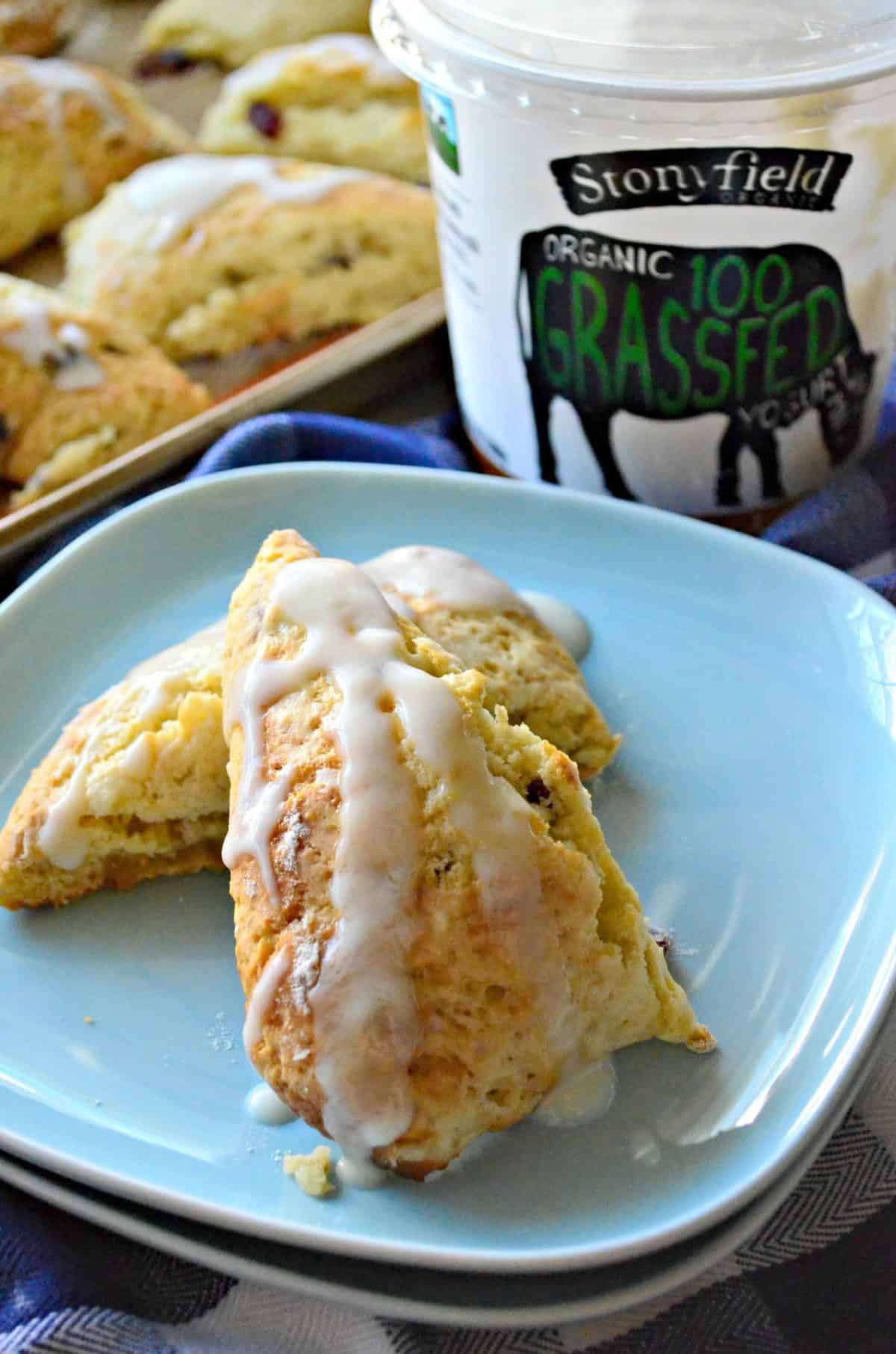 Closeup sliced and stacked scone with white glaze icing drizzled on light blue plate in front of stonyfield yogurt.