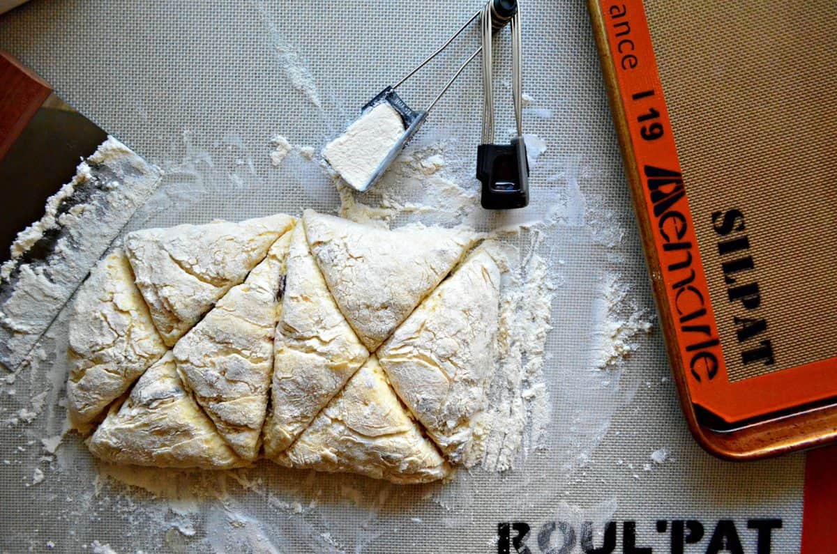 Top view of unbaked but floured Cranberry Vanilla Yogurt Scones on baking mat next to measuring cup of flour.