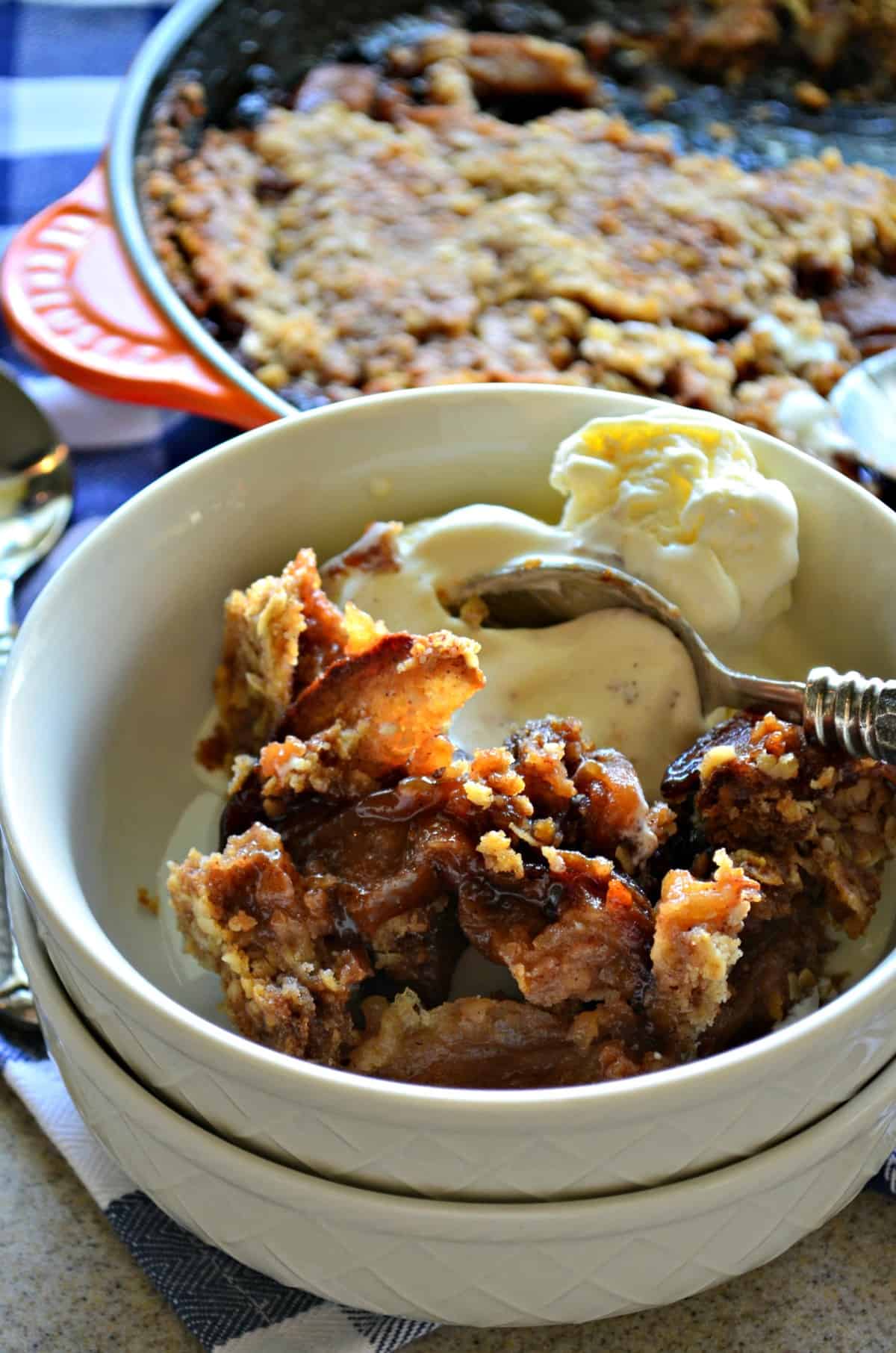 closeup small white bowl of Apple Crisp with vanilla ice cream and spoon.