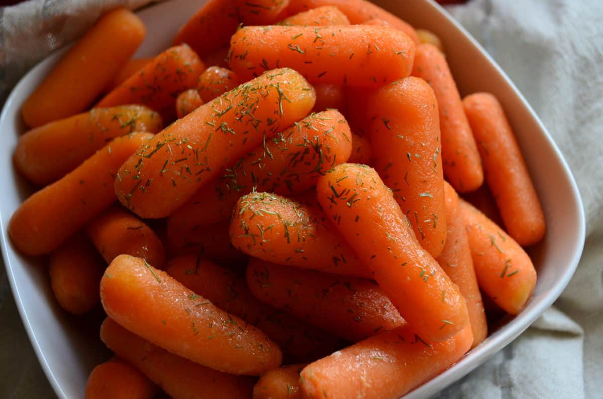 Close up Slow Cooker Honey Glazed Carrots with dried herbs in white bowl on tablecloth.