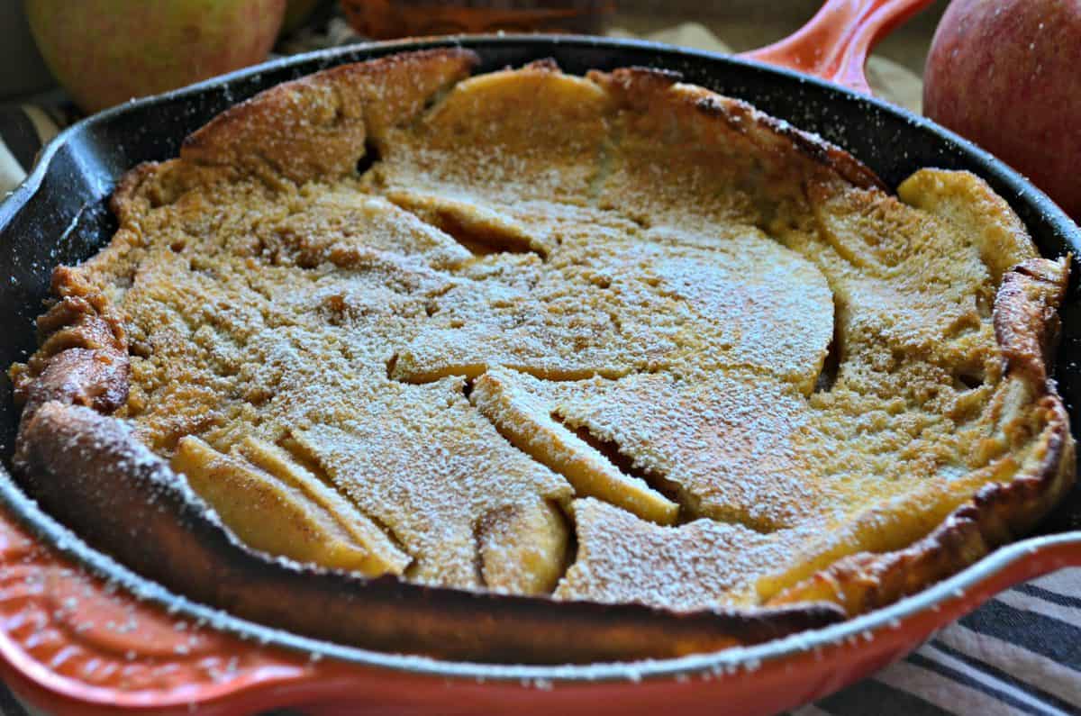 top view of pancake-like pastry with apple slices baked in skillet, topped with powdered sugar.