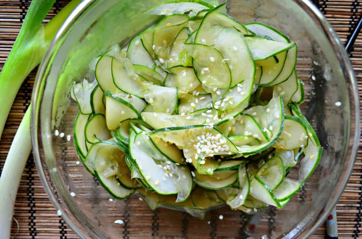 Over head shot of a thinly sliced cucumbers with sesame seeds in a glass bowl.