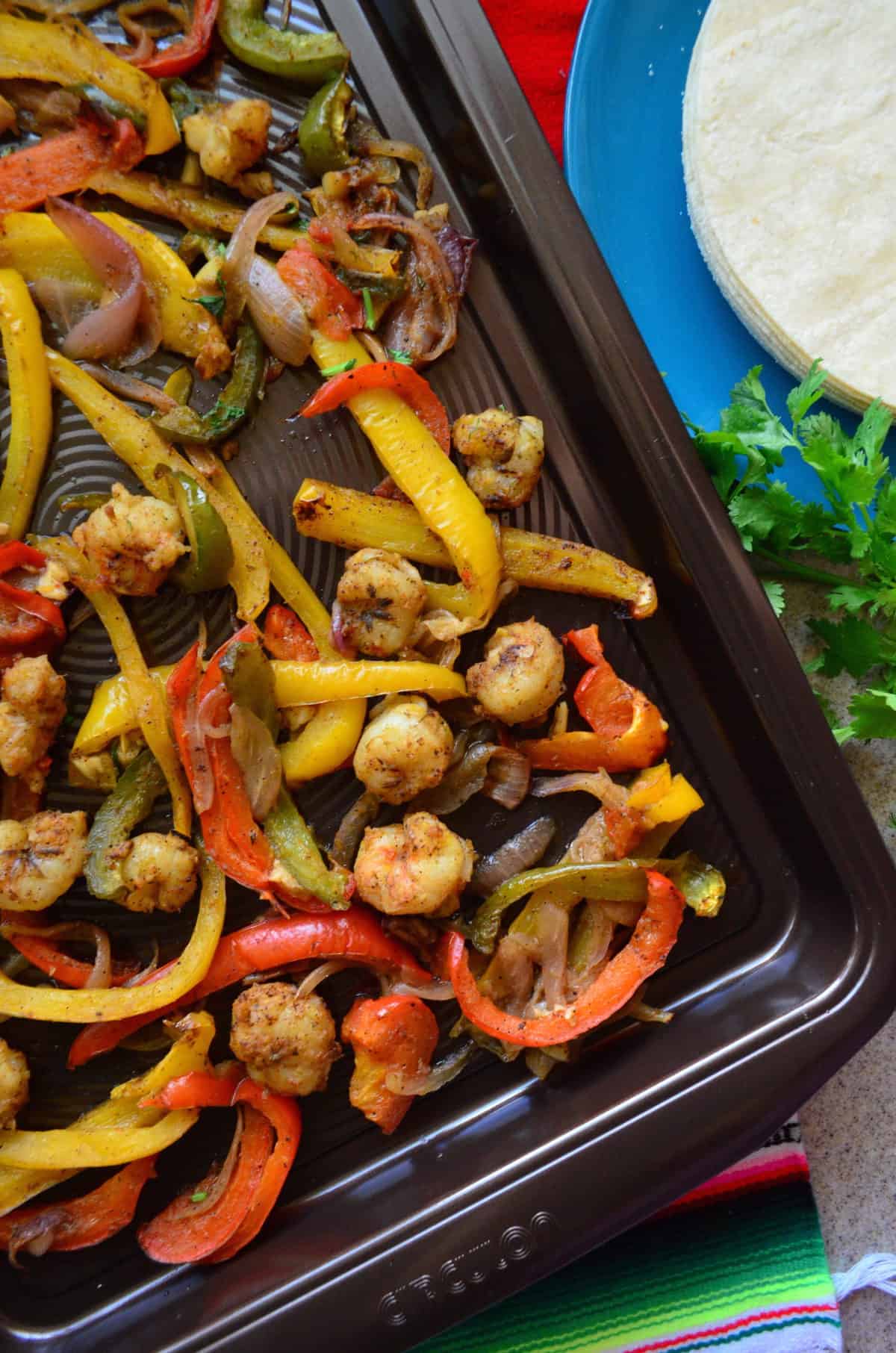 top view close up of seasoned shrimp, sliced bell peppers, and onions on a sheet pan.