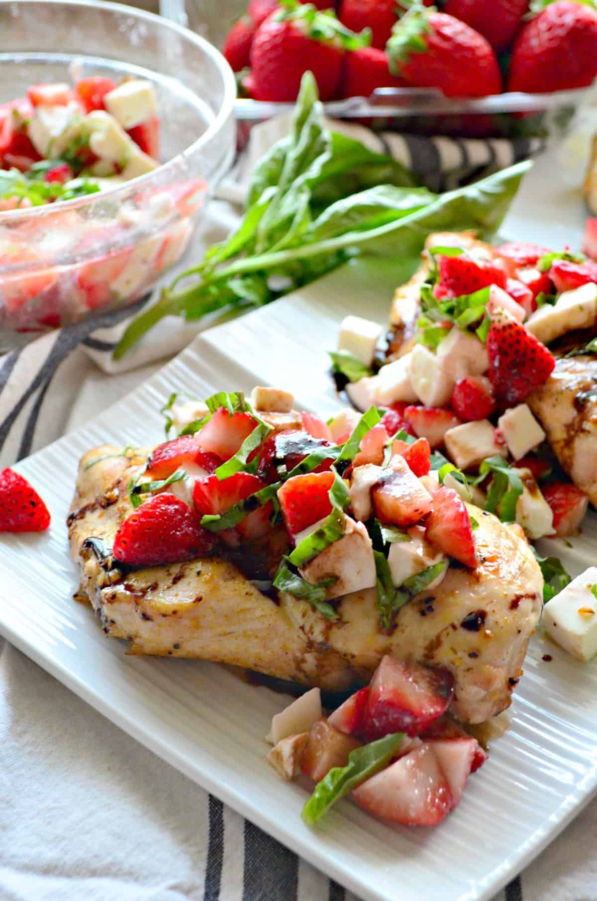 closeup grilled chicken topped with basil, strawberries, and balsamic sauce on platter near ingredients.