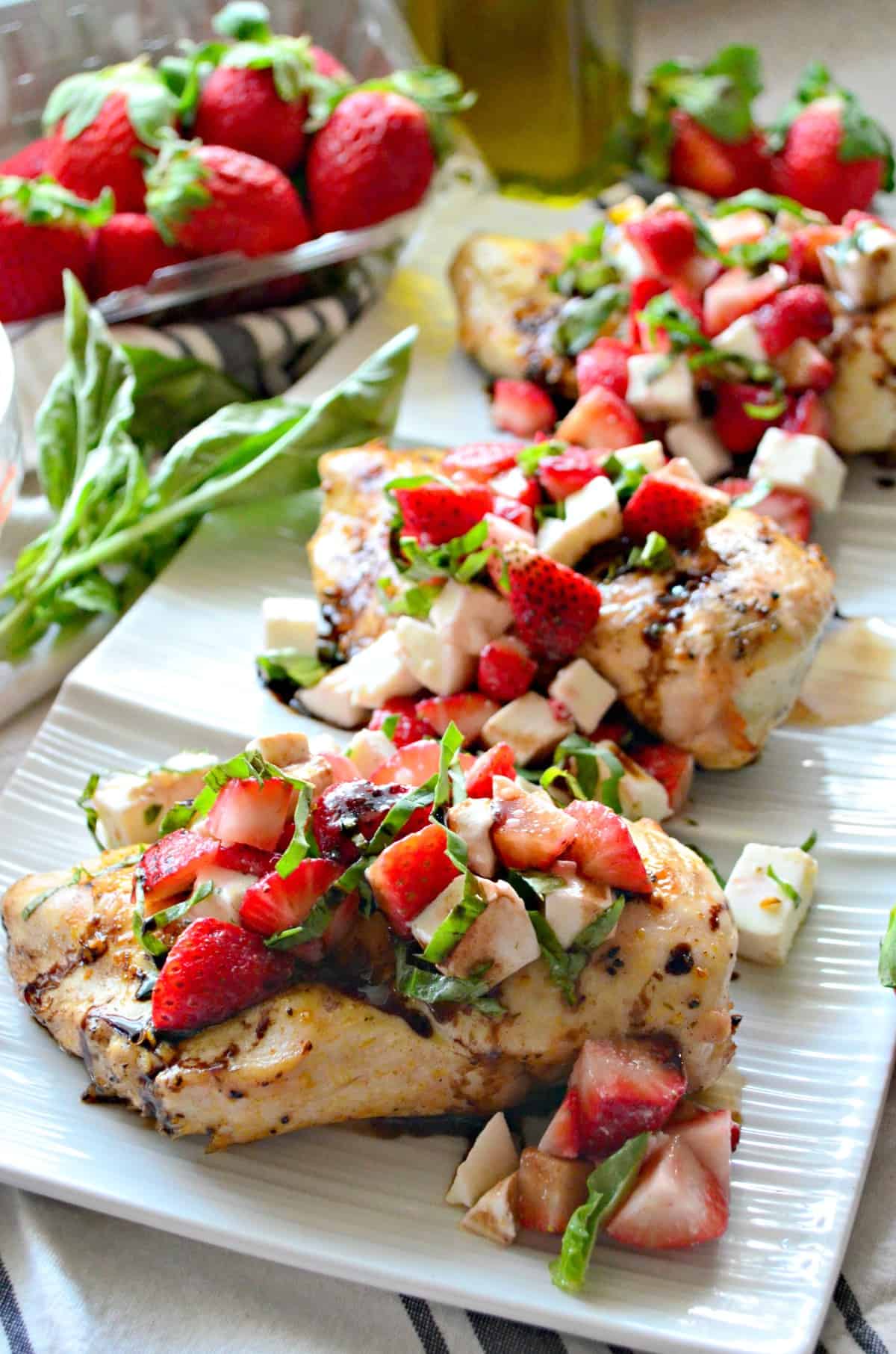 closeup front view of grilled chicken topped with basil, strawberries, and balsamic sauce on rectangular platter.