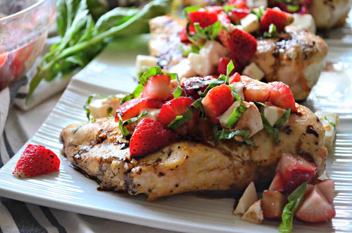 grilled chicken topped with basil, strawberries, and balsamic sauce on rectangular white platter.