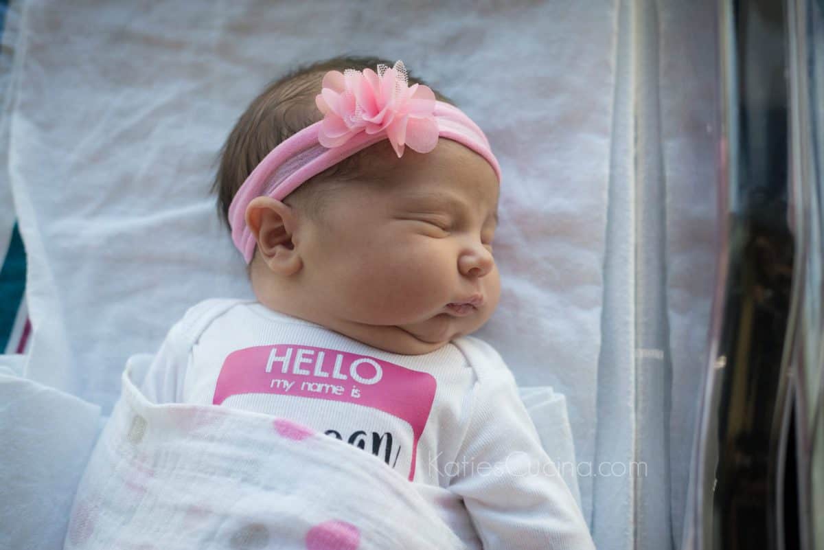 Newborn Photo of Katie's baby girl with a pink flower hair band on her head.