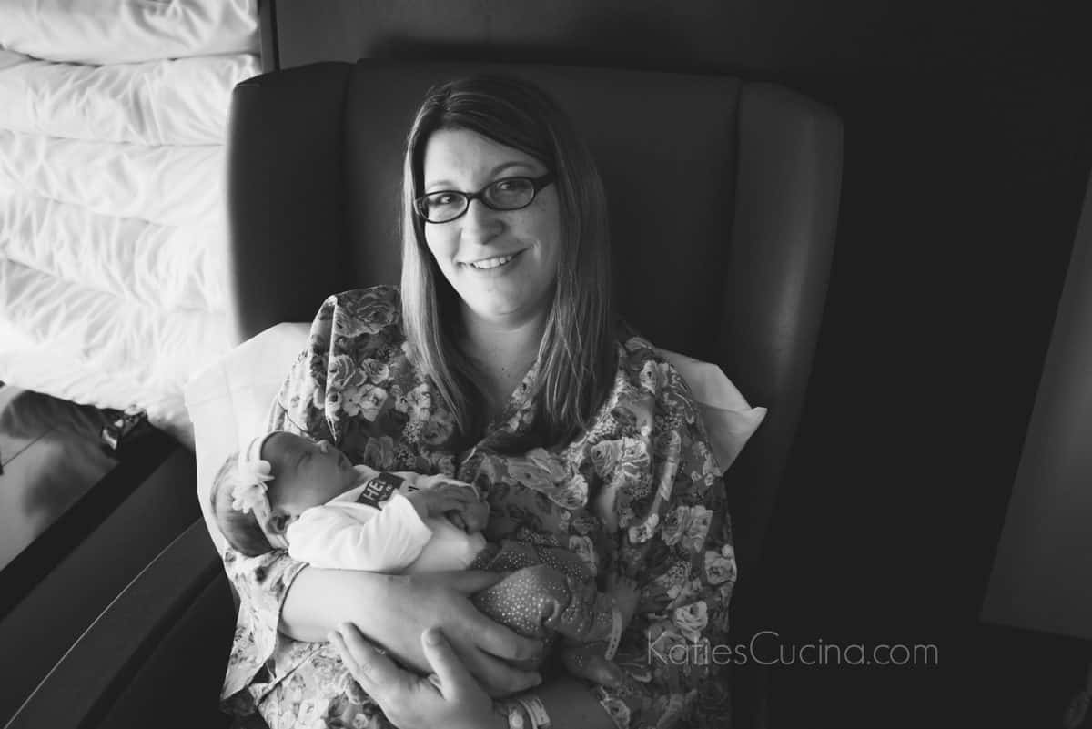 black and white photo of new mother wearing glasses and cozy clothes holding a newborn baby girl.