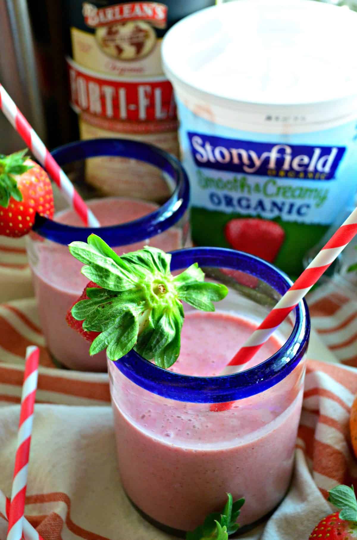 closeup two blue rimmed glasses with red pink blended drink rimmed with fresh strawberries.