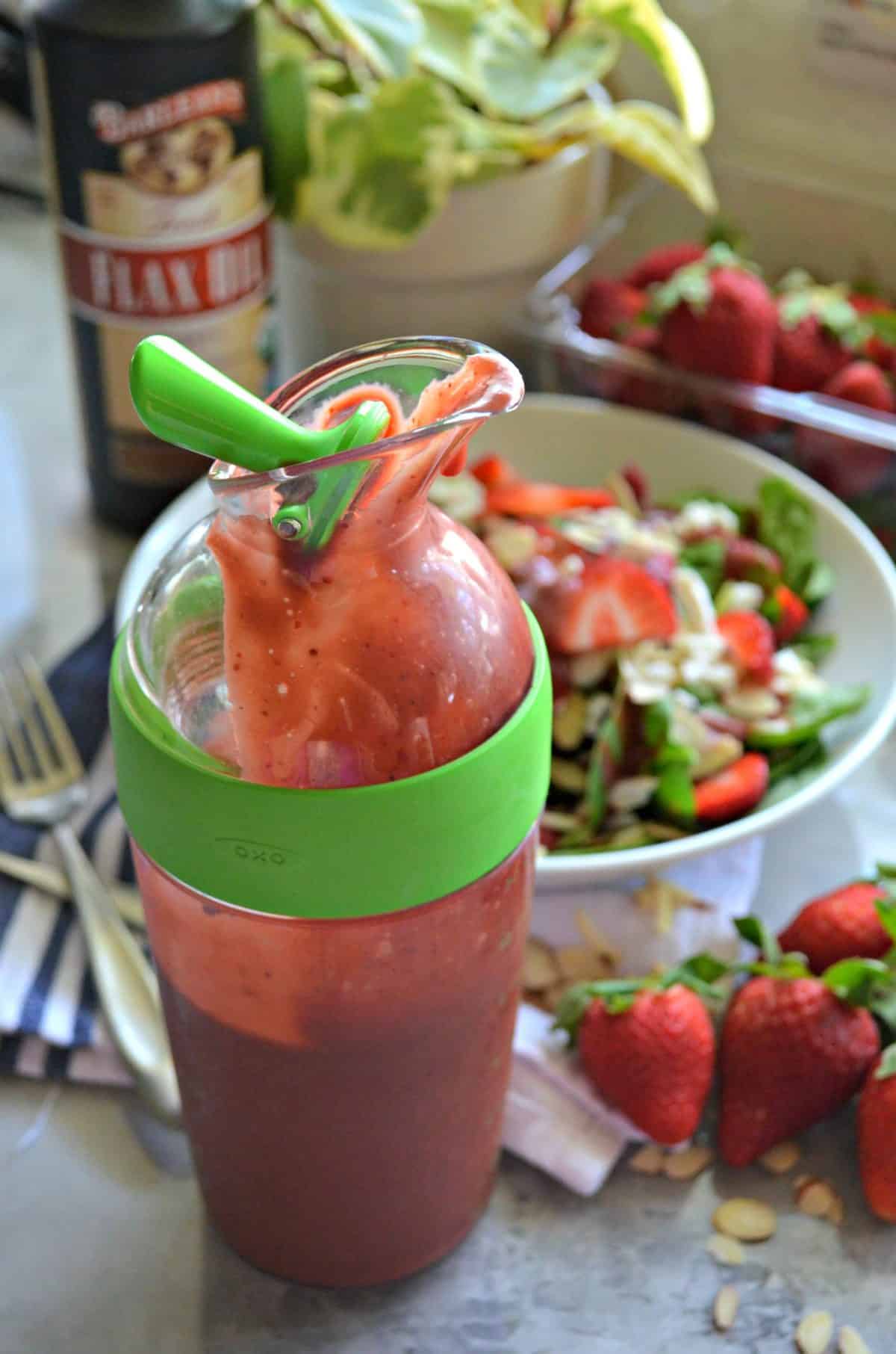 salad dressing container filled with pink seedy liquid in front of bowl filled with salad.