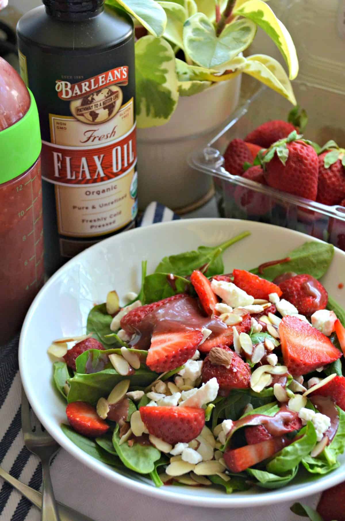 spinach salad with strawberries, almond slivers, dressing, and feta in white bowl with title text.