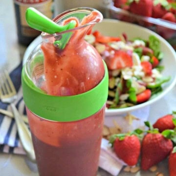 Clear salad dressing holder with green ring with a pink salad dressing in the shaker.