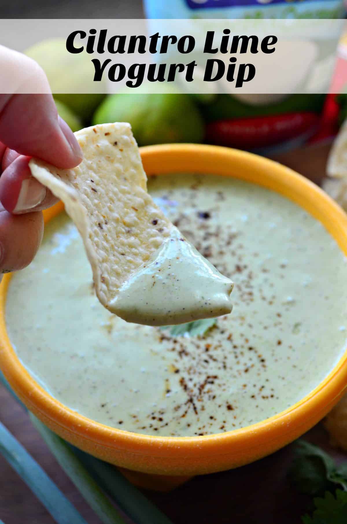 close up of hand dipping corn tortilla chip into Creamy Cilantro Lime Yogurt Dip from yellow bowl with title text.