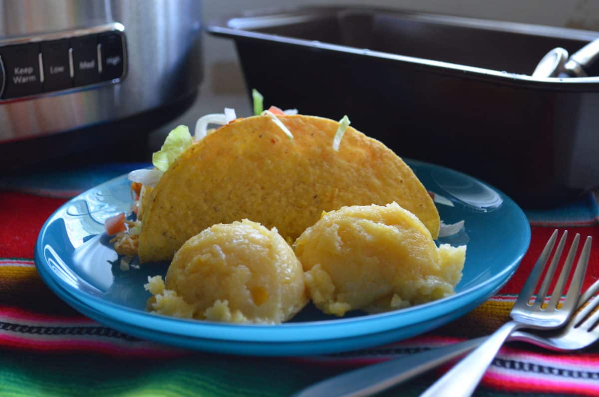 Hard shell taco with tomatoes and lettuce showing plated with two corn cakes on tablecloth with forks.