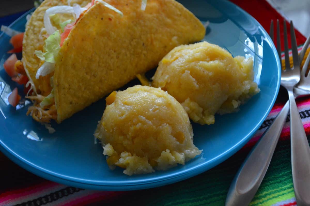 close up of hard shell taco with tomatoes and lettuce showing plated with two corn cakes on tablecloth.