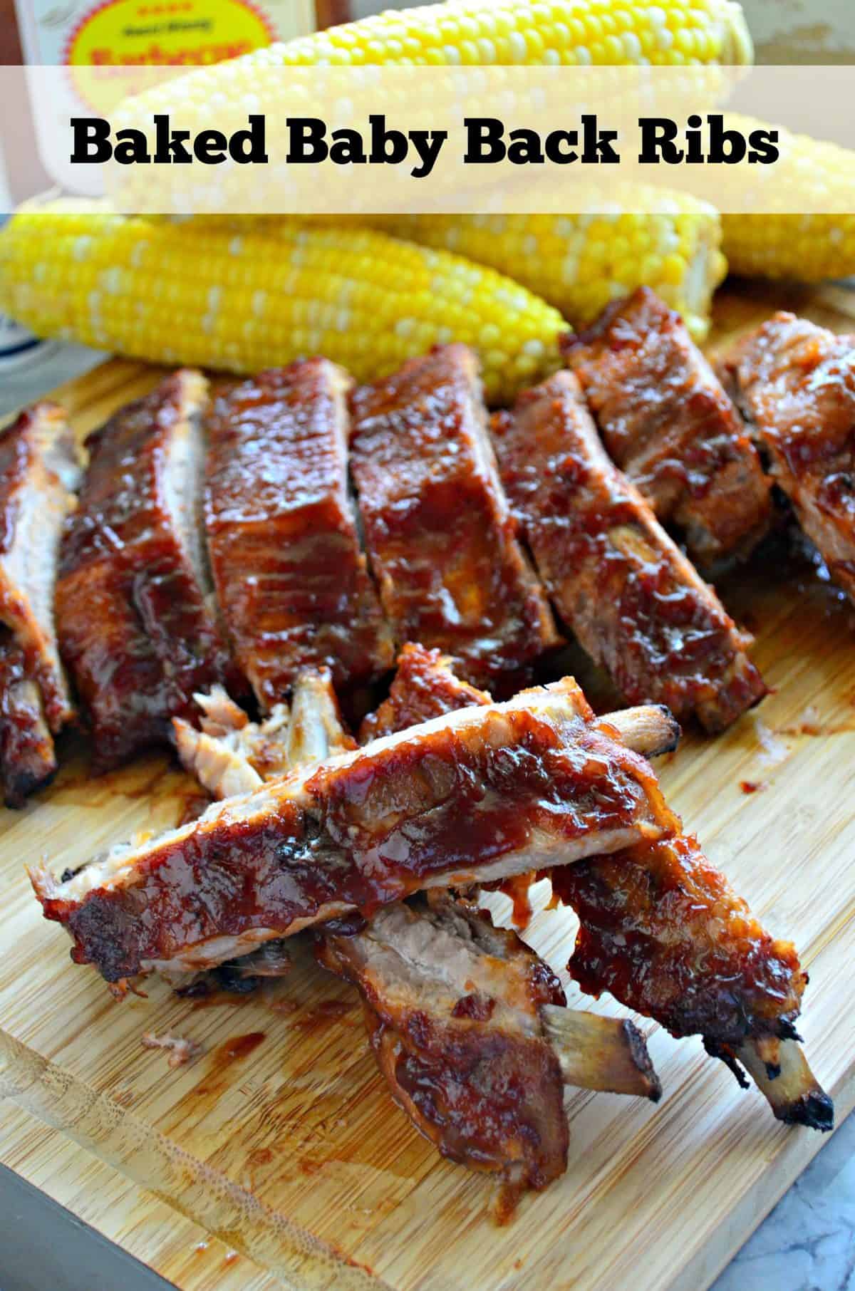 baby back ribs smothered in red sauce and stacked on cutting board in front of fresh corn with title text.