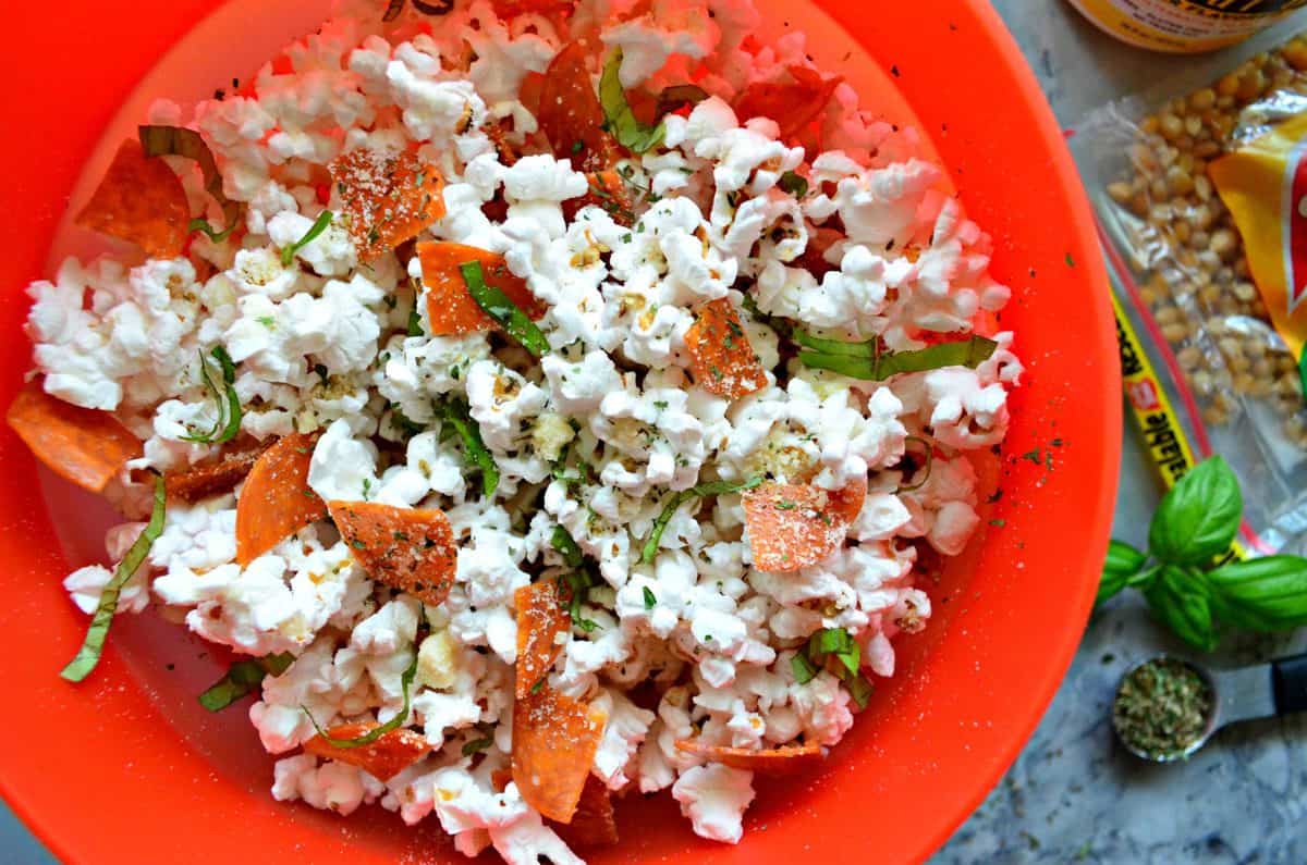 top view bowl of quartered pepperoni, basil, and seasonings on popcorn.