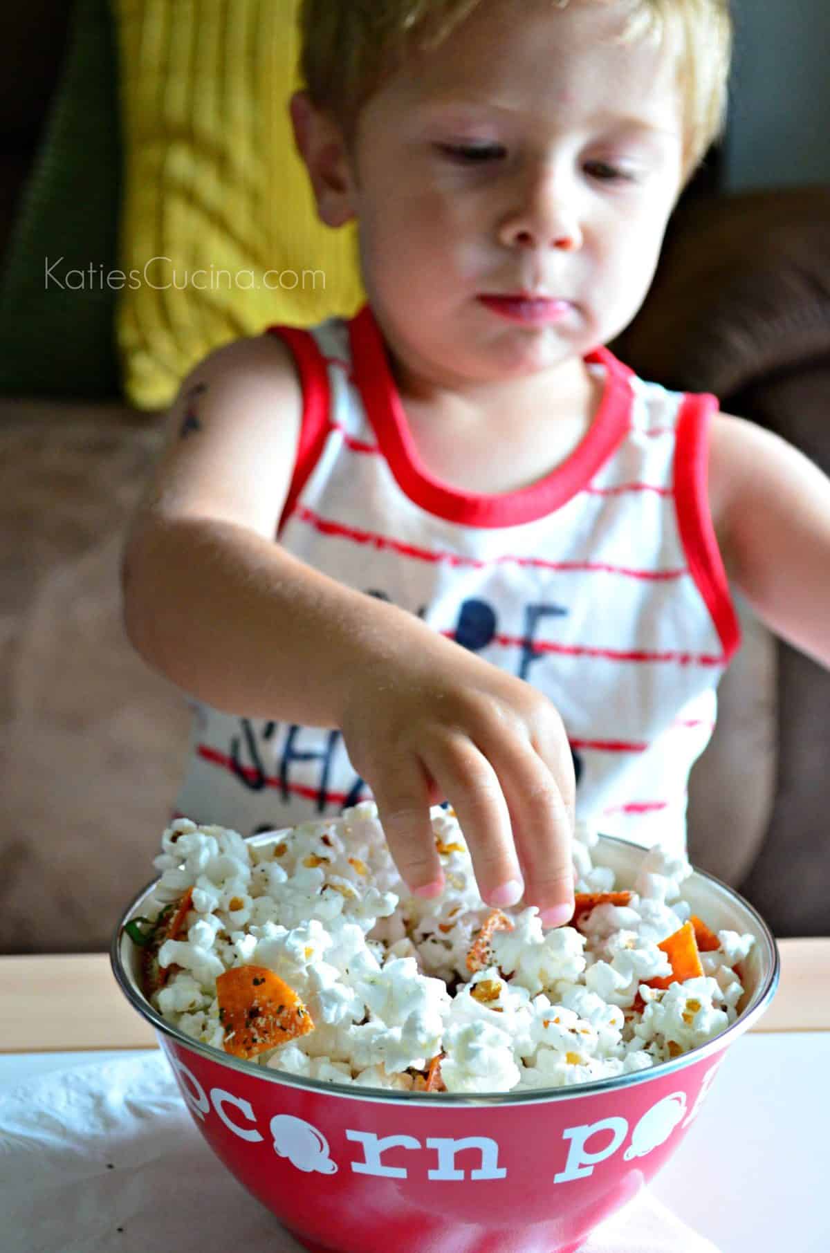 young boy reaching his hand into bowl of pizza popcorn.