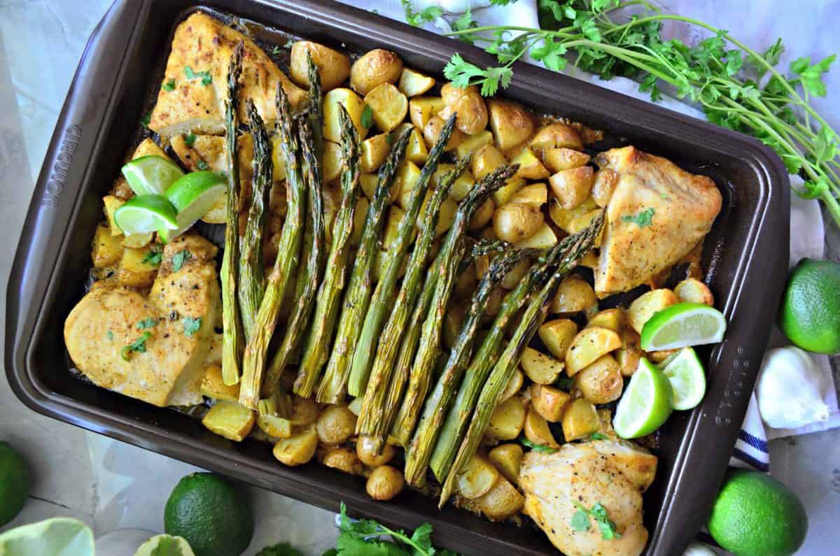 top view pan of small potatoes, asparagus, chicken, and lime next to garlic, lime, and cilantro.