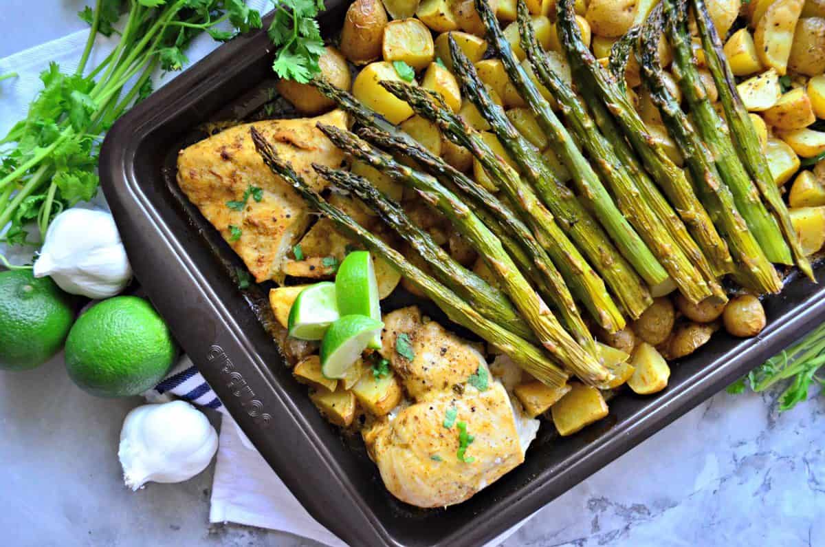 top view pan of small potatoes, asparagus, chicken, and lime next to garlic, lime, and cilantro.