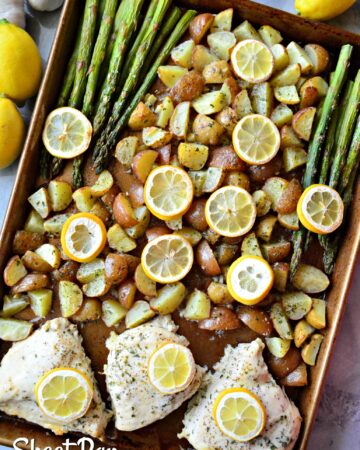 Top view of a brown sheet pan with diced ptoatoes, asparagus, and chicken breast with lemon wedges.